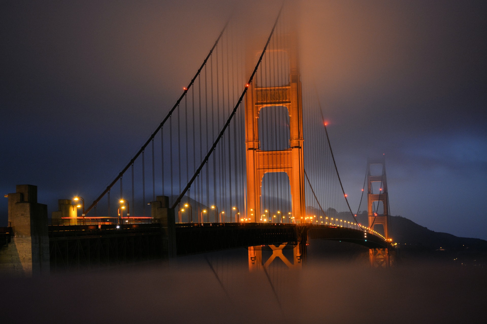 Golden Gate Bridge in the fog lit up at night