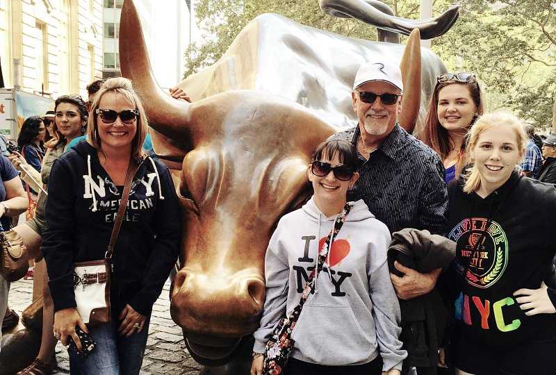father mother and three daughters stand near the charging bull statue in the Financial District