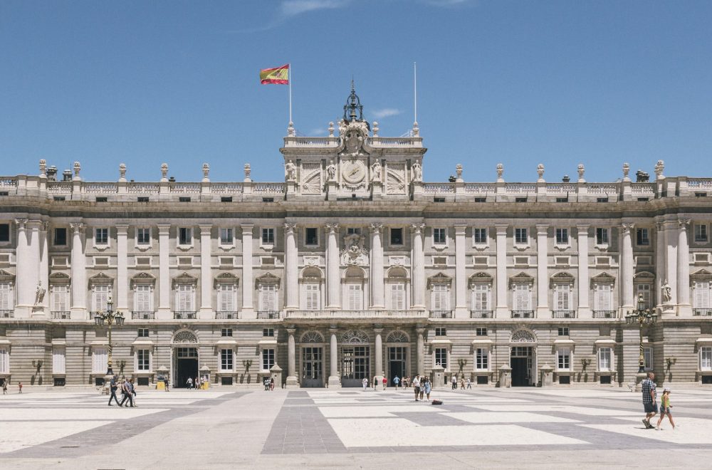 a large building with columns and a flag on top with Royal Palace of Madrid in the background