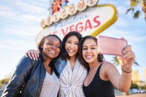 three friends on vacation taking a group selfie in front of the welcome to las vegas sign